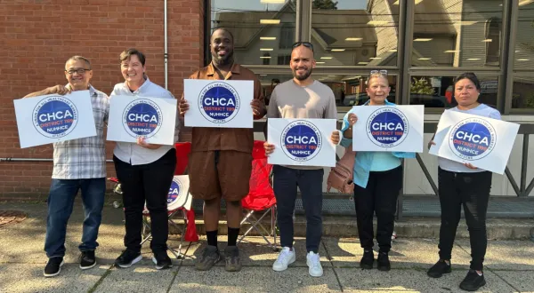 Members standing together holding CHCA signs in the sun.